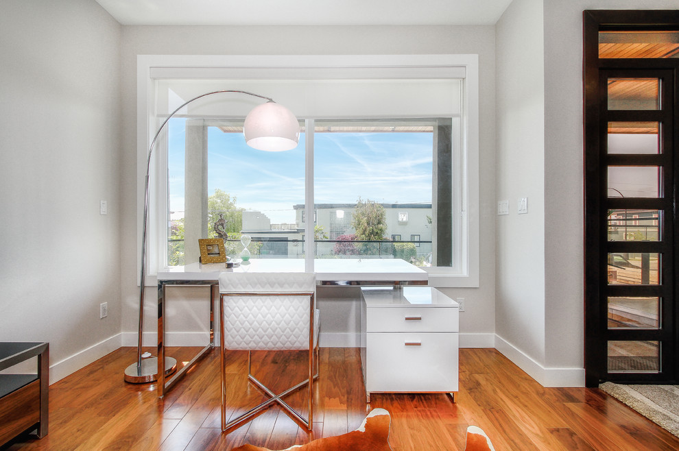 Ejemplo de despacho actual con paredes grises, suelo de madera en tonos medios y escritorio independiente