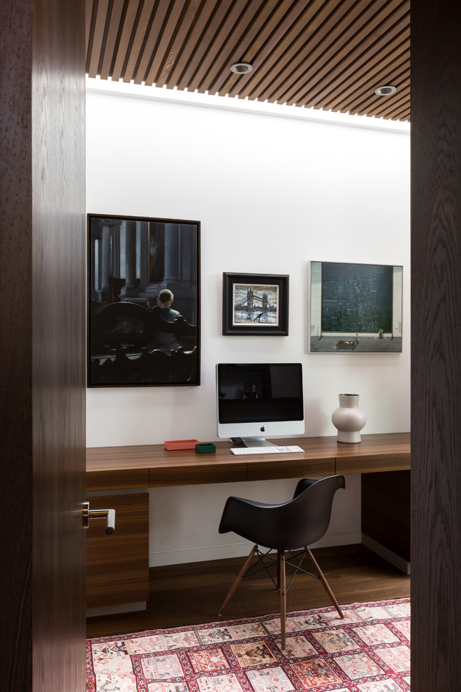 Diseño de despacho contemporáneo de tamaño medio con paredes blancas, escritorio empotrado, suelo marrón y suelo de madera oscura