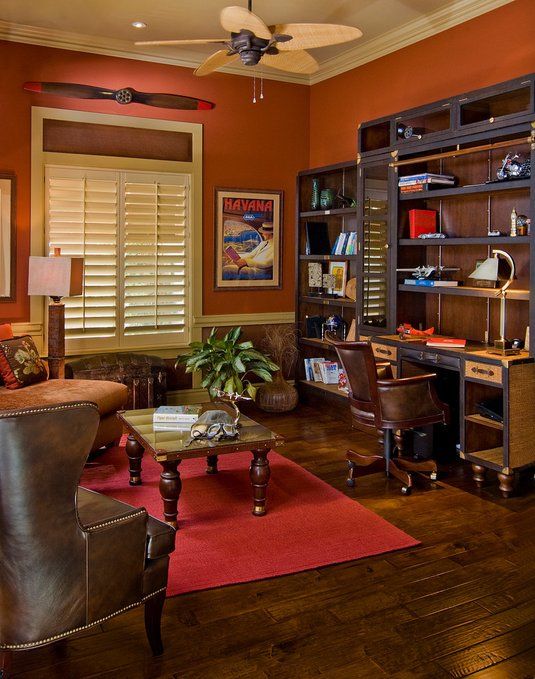 Foto di un grande studio tropicale con libreria, pareti rosse, parquet scuro, scrivania autoportante e pavimento marrone