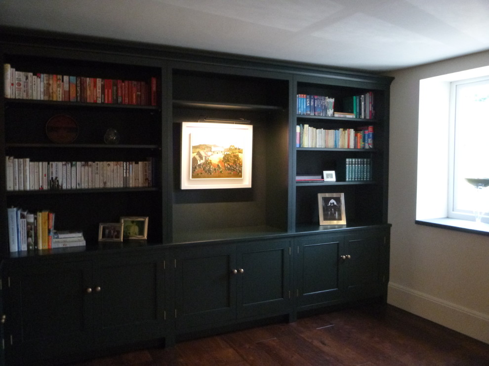 Klassisk inredning av ett mellanstort hemmabibliotek, med gröna väggar, mörkt trägolv, en standard öppen spis och en spiselkrans i sten