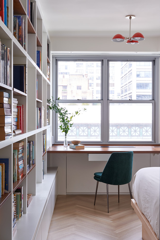 Inspiration for a contemporary home office in New York with a reading nook, white walls, light hardwood flooring, a built-in desk, beige floors and feature lighting.