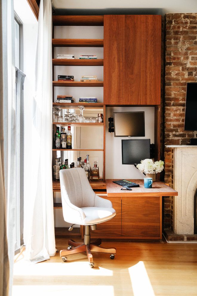 Imagen de despacho de estilo de casa de campo pequeño con escritorio empotrado, suelo de madera clara, todas las chimeneas y marco de chimenea de ladrillo