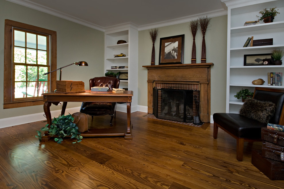 Medium sized rural home office in Raleigh with green walls, medium hardwood flooring, a standard fireplace, a wooden fireplace surround, a freestanding desk and brown floors.