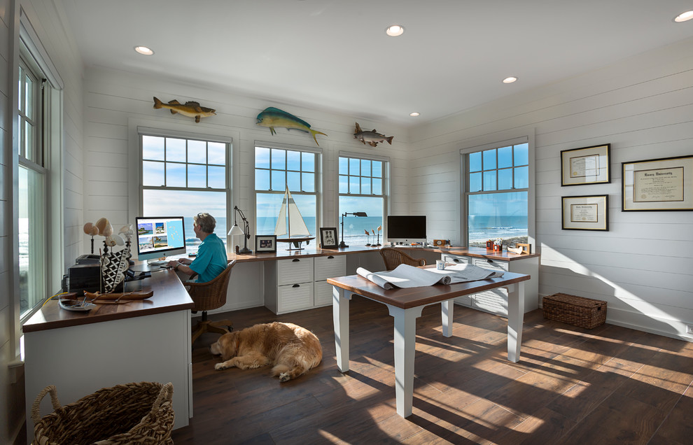 Ejemplo de despacho costero con paredes blancas, suelo de madera oscura y escritorio empotrado