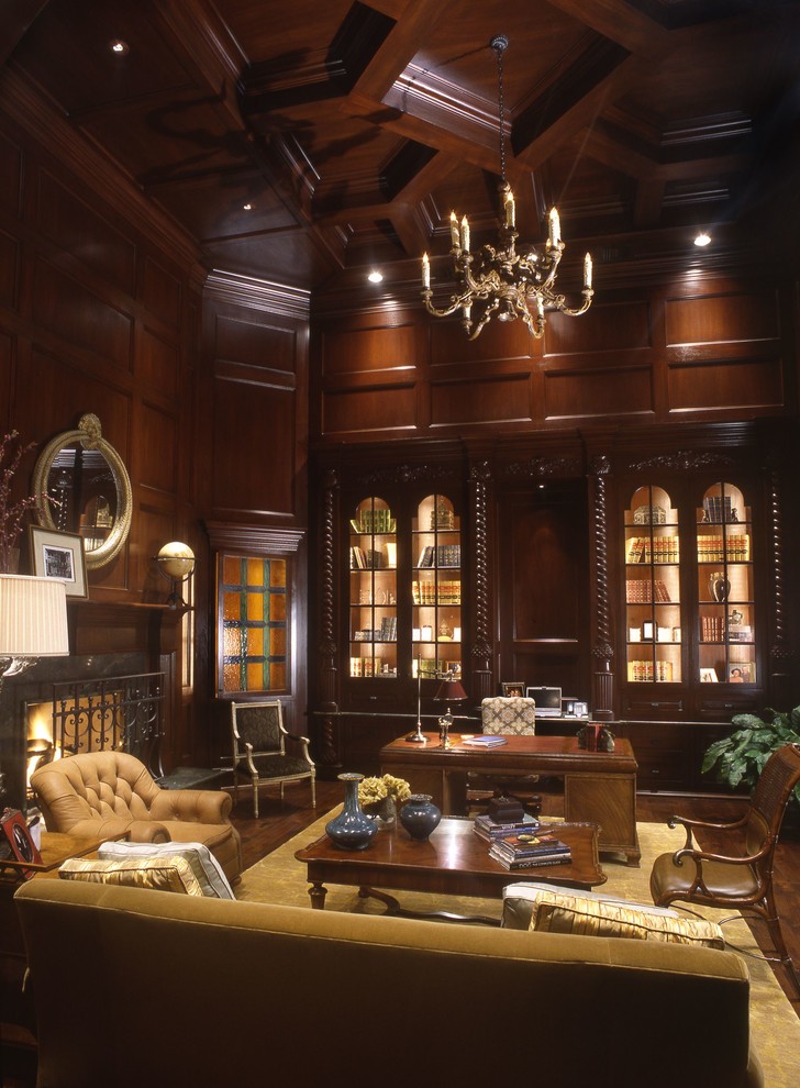 Klassisk inredning av ett stort hemmabibliotek, med bruna väggar, en standard öppen spis, en spiselkrans i trä och ett fristående skrivbord