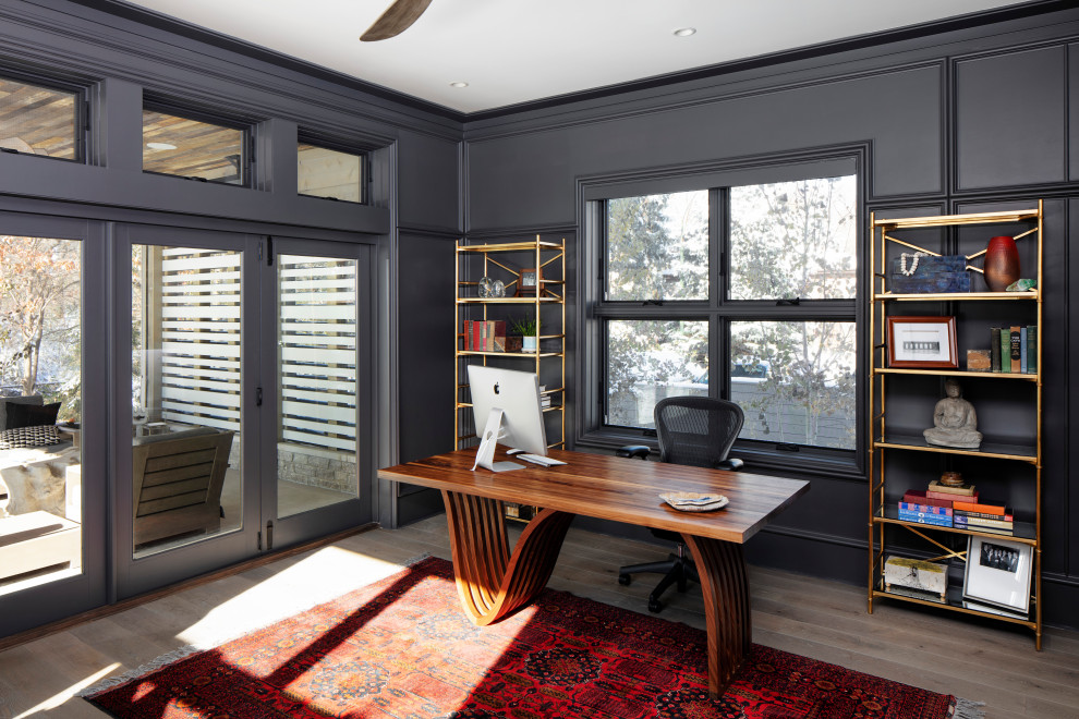 Diseño de despacho costero con paredes negras, suelo de madera en tonos medios, escritorio independiente y panelado