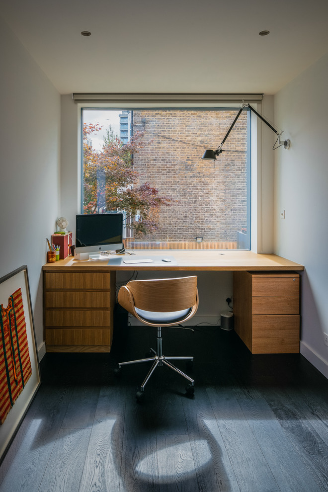 Modernes Arbeitszimmer mit Arbeitsplatz, weißer Wandfarbe, dunklem Holzboden, freistehendem Schreibtisch und schwarzem Boden in London