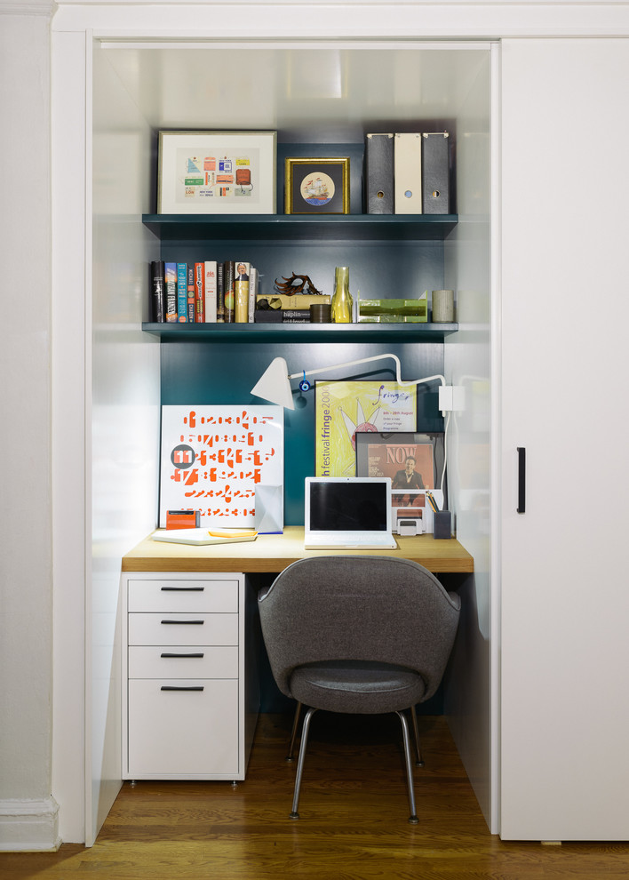 Modern inredning av ett litet arbetsrum, med blå väggar, mellanmörkt trägolv och ett inbyggt skrivbord