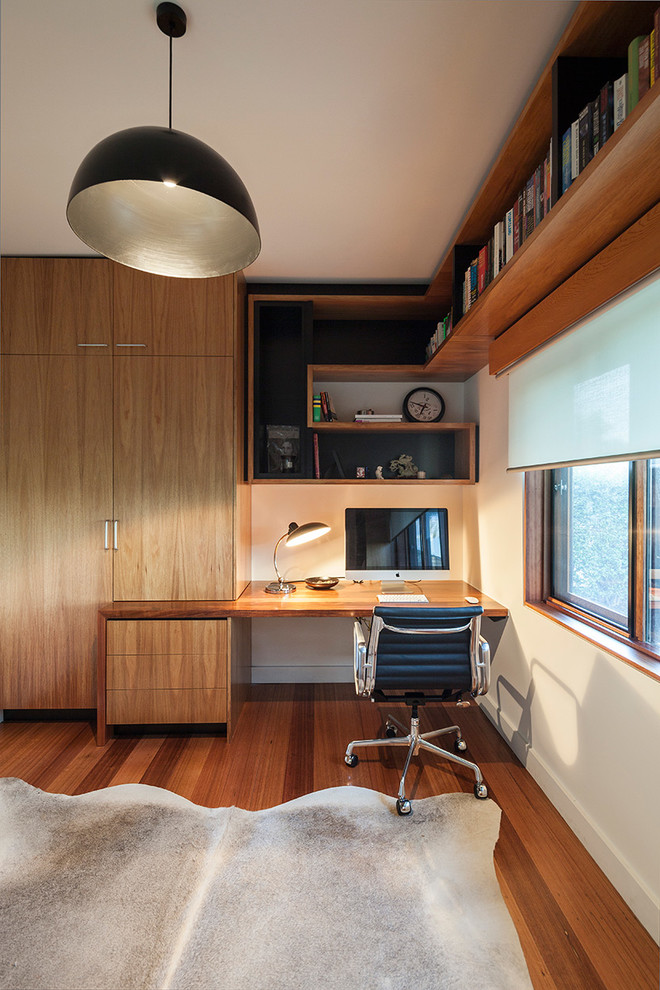 Cette image montre un petit bureau design avec un mur blanc, un sol en bois brun et un bureau intégré.