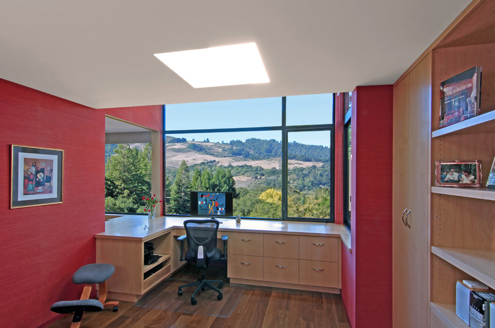 Modelo de despacho minimalista de tamaño medio sin chimenea con paredes rojas, suelo de madera en tonos medios y escritorio empotrado