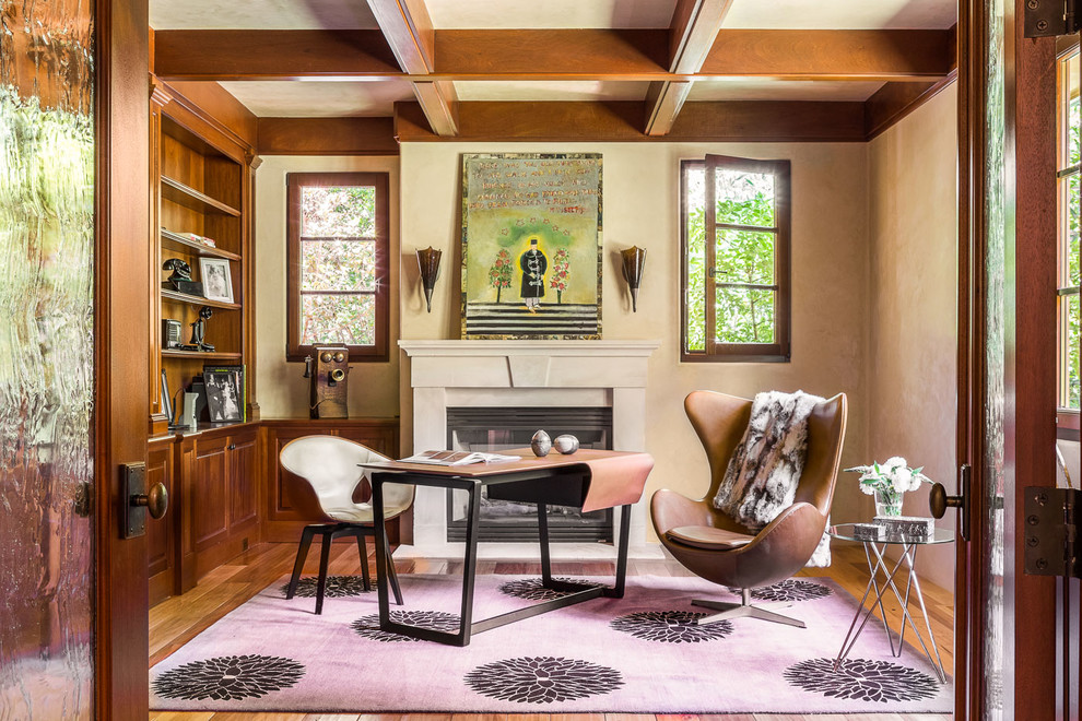 Bild på ett stort eklektiskt hemmabibliotek, med en standard öppen spis, en spiselkrans i betong, ett fristående skrivbord, beige väggar, mellanmörkt trägolv och brunt golv