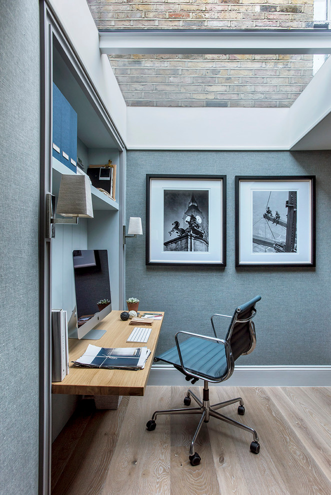 This is an example of a small modern home office with blue walls, light hardwood flooring, a built-in desk and beige floors.