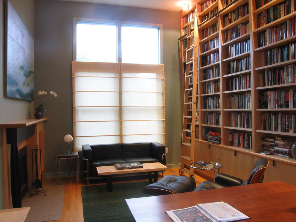 На фото: домашняя библиотека среднего размера в современном стиле с зелеными стенами, светлым паркетным полом, стандартным камином, фасадом камина из дерева и отдельно стоящим рабочим столом