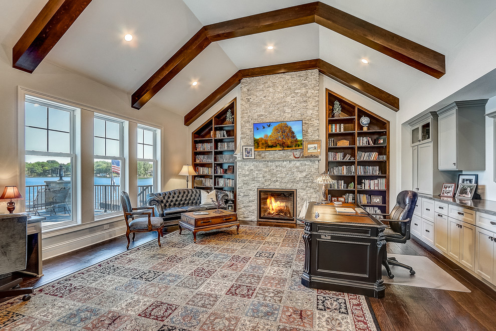 Huge beach style freestanding desk dark wood floor and brown floor home office library photo in Milwaukee with white walls, a standard fireplace and a stone fireplace