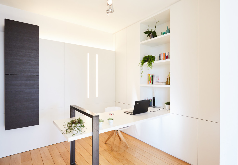 Idéer för funkis hemmabibliotek, med vita väggar, mellanmörkt trägolv och ett inbyggt skrivbord