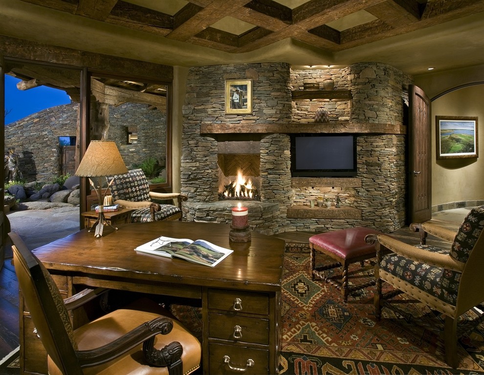Imagen de despacho rural grande con paredes beige, todas las chimeneas, marco de chimenea de piedra y escritorio independiente
