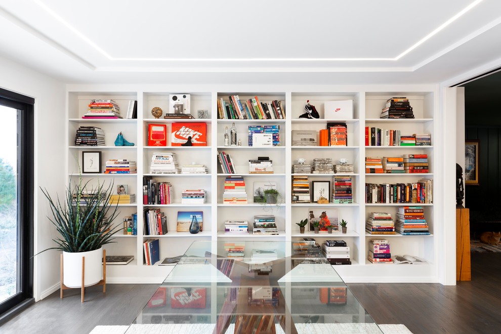 Inspiration för stora moderna hemmabibliotek, med vita väggar, mörkt trägolv, en standard öppen spis, en spiselkrans i trä, ett fristående skrivbord och grått golv