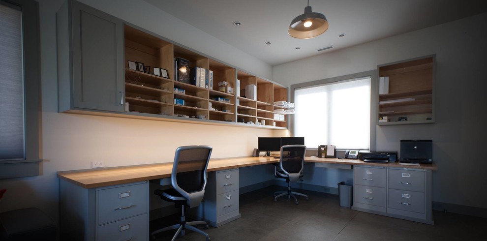 Cette image montre un très grand bureau craftsman avec un mur blanc, sol en béton ciré et un bureau intégré.