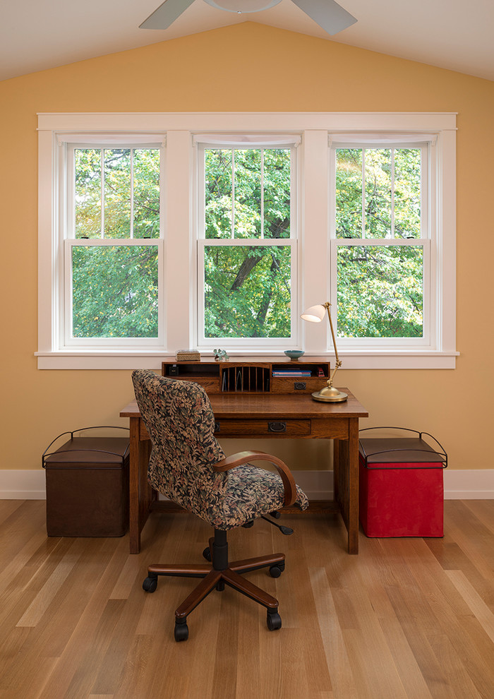 Idéer för mellanstora amerikanska hemmabibliotek, med gula väggar, mellanmörkt trägolv, ett fristående skrivbord och beiget golv