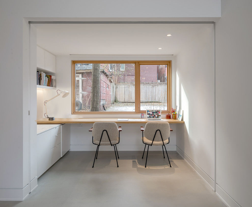 Ejemplo de despacho minimalista con paredes blancas, suelo de cemento y escritorio empotrado