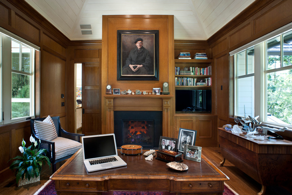 Inredning av ett klassiskt mellanstort hemmabibliotek, med mellanmörkt trägolv, en standard öppen spis, ett fristående skrivbord och en spiselkrans i sten