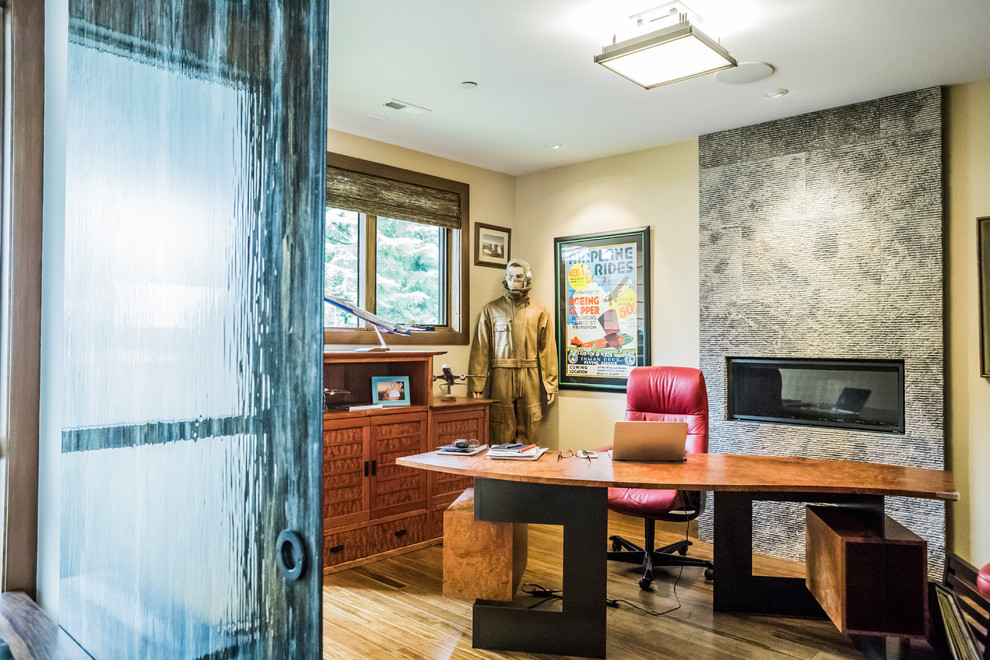 シアトルにある高級な中くらいなミッドセンチュリースタイルのおしゃれな書斎 (ベージュの壁、無垢フローリング、横長型暖炉、石材の暖炉まわり、自立型机、茶色い床) の写真
