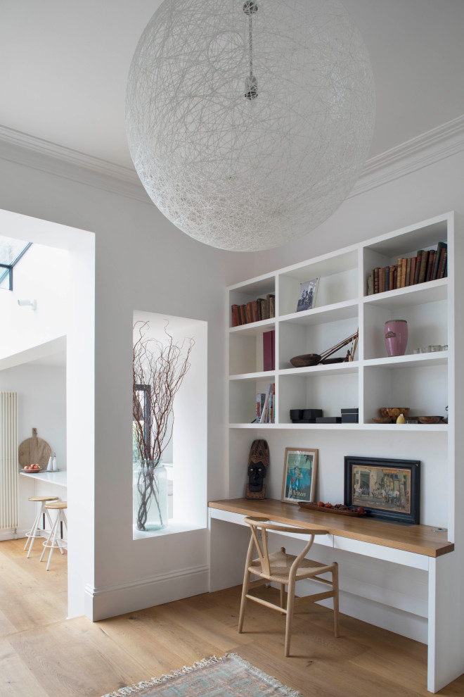 This is an example of a medium sized contemporary study in London with white walls, medium hardwood flooring, a built-in desk and beige floors.