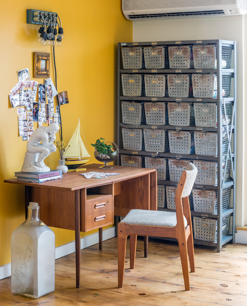 Eklektisk inredning av ett arbetsrum, med gula väggar, mellanmörkt trägolv och ett fristående skrivbord