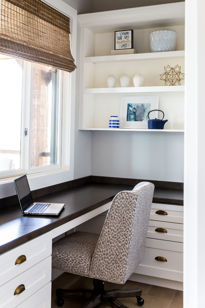 Ejemplo de despacho de estilo de casa de campo con paredes blancas, suelo de madera clara y escritorio empotrado