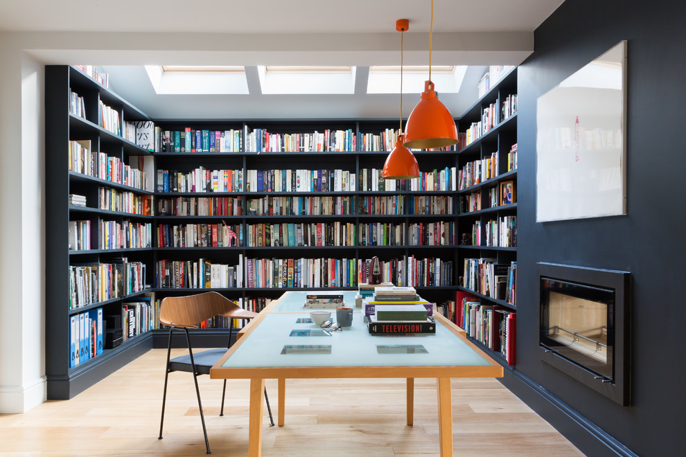 Idéer för stora funkis hemmabibliotek, med grå väggar, mellanmörkt trägolv, en spiselkrans i metall, ett fristående skrivbord och en bred öppen spis