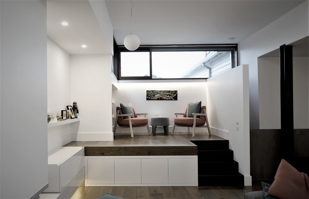 Mittelgroßes Modernes Lesezimmer mit weißer Wandfarbe, braunem Holzboden, Gaskamin und Kaminumrandung aus Beton in Melbourne