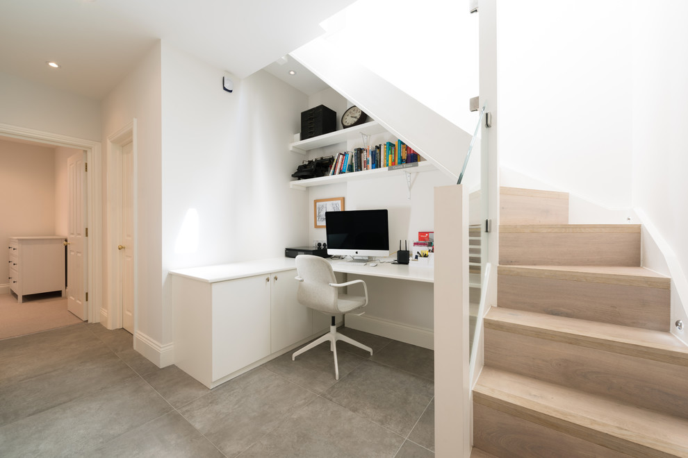 Photo of a contemporary study in London with white walls, a built-in desk and grey floors.
