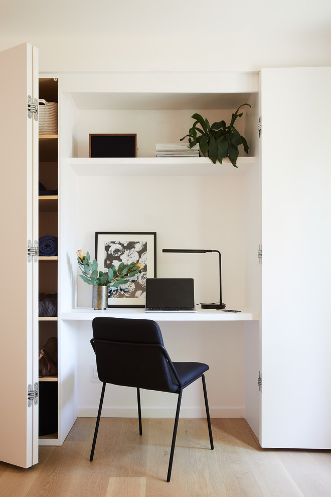 Exempel på ett modernt arbetsrum, med vita väggar, ljust trägolv och ett inbyggt skrivbord