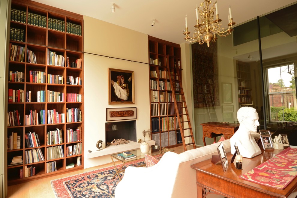 Foto på ett stort vintage arbetsrum, med ett bibliotek, beige väggar, ljust trägolv, en bred öppen spis och en spiselkrans i gips