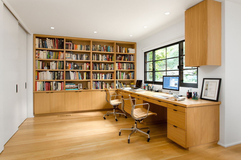 Foto på ett mellanstort retro hemmabibliotek, med vita väggar, ljust trägolv, ett inbyggt skrivbord och gult golv