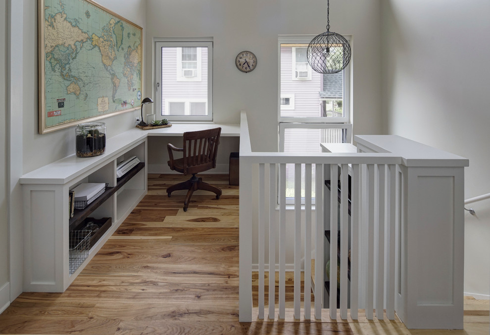 This is an example of a modern home office in Chicago with white walls, medium hardwood flooring and a built-in desk.