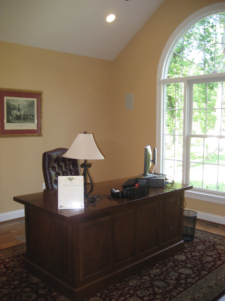 Immagine di un ufficio classico di medie dimensioni con pareti gialle, pavimento in legno massello medio, scrivania autoportante e pavimento marrone