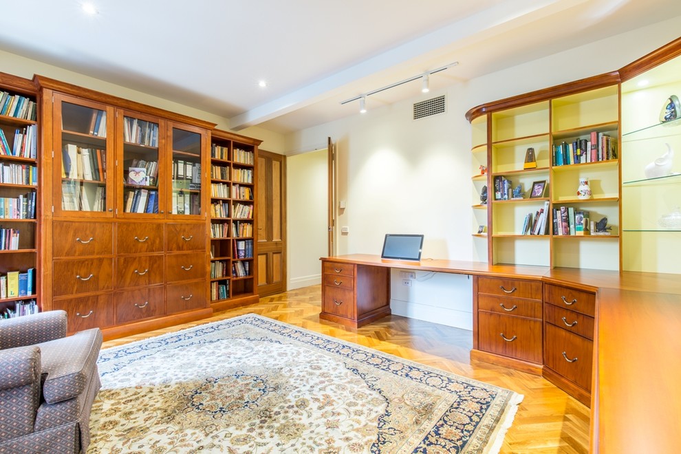 Idéer för ett stort klassiskt hemmabibliotek, med vita väggar, mellanmörkt trägolv och ett inbyggt skrivbord