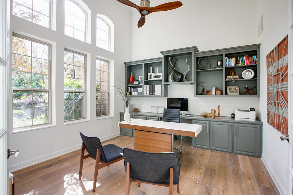 Modelo de despacho clásico renovado grande sin chimenea con paredes blancas, suelo de madera clara y escritorio independiente