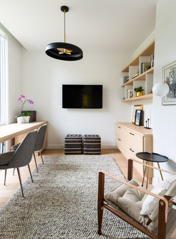 Modelo de despacho actual de tamaño medio con paredes blancas, suelo de madera clara, escritorio empotrado y suelo beige