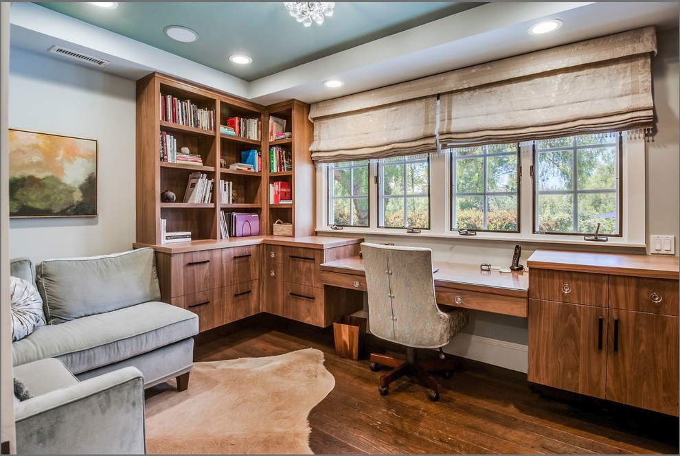Diseño de despacho actual con paredes blancas, suelo de madera oscura, escritorio empotrado y suelo marrón
