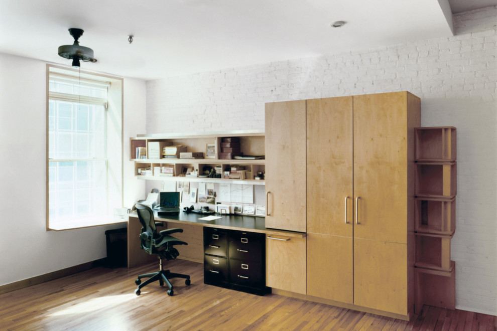 Photo of a small home office in New York with white walls, light hardwood flooring and a built-in desk.