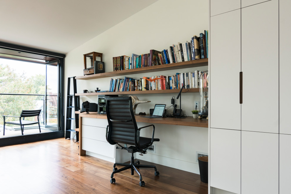 Medium sized modern home office in Toronto with white walls, medium hardwood flooring, no fireplace, a built-in desk and brown floors.