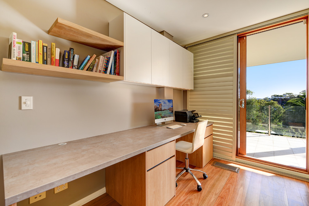 Imagen de despacho actual de tamaño medio con paredes grises, suelo de madera en tonos medios, escritorio empotrado y suelo marrón