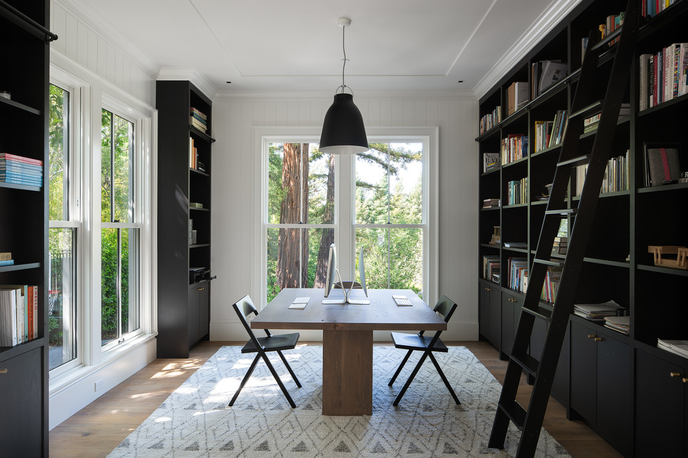 Стильный дизайн: большой домашняя библиотека в современном стиле с белыми стенами, паркетным полом среднего тона, отдельно стоящим рабочим столом и коричневым полом без камина - последний тренд