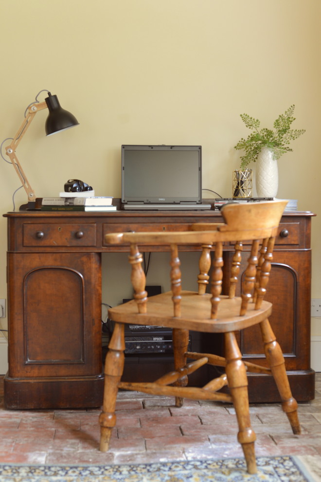 This is an example of a medium sized country study in Sussex with white walls, brick flooring and a freestanding desk.