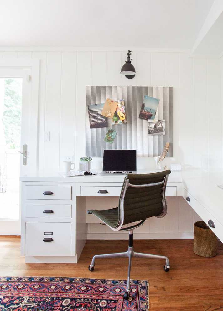 Eklektisk inredning av ett arbetsrum, med ett inbyggt skrivbord, mellanmörkt trägolv och vita väggar