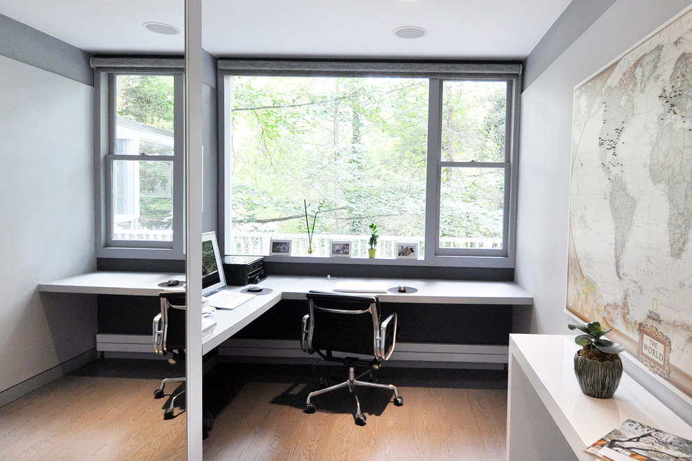 This is an example of a small modern study in New York with grey walls, a built-in desk, light hardwood flooring and no fireplace.