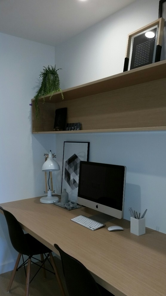 This is an example of a small contemporary home studio in Melbourne with white walls, light hardwood flooring and a built-in desk.