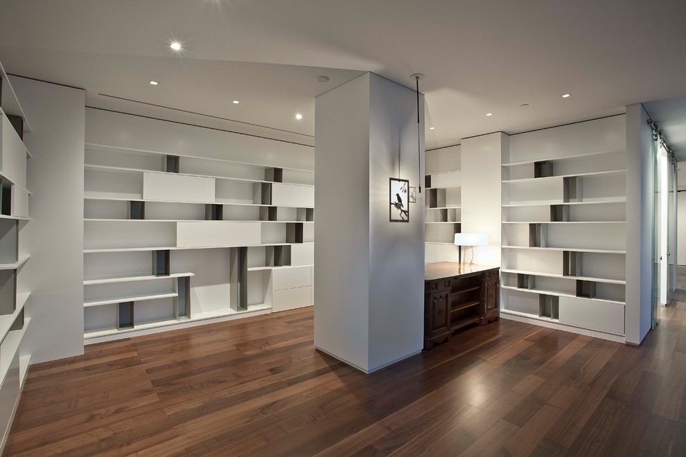 Cette photo montre un grand bureau moderne avec une bibliothèque ou un coin lecture, un mur blanc, un sol en bois brun, aucune cheminée, un bureau indépendant et un sol marron.